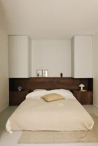 A well-lit bedroom with a bed, nightstand, and dresser, featuring a white comforter, brown pillow, and wooden furniture