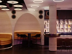 A well-lit restaurant interior with a bar, dining area, and modern decor, featuring a variety of books on the walls