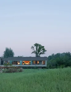A modern house with a large open living room and kitchen, surrounded by a lush green field, with natural light and a peaceful atmosphere