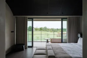 A well-lit living room with a couch, chair, and dining table, featuring a large window with a view of the outdoors and a mix of wood and metal materials