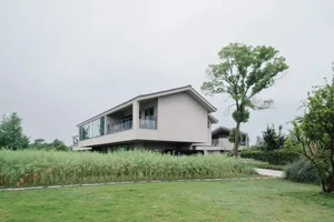 一座現代住宅，白色外觀，周圍環繞翠綠田野，擁有大片窗戶與數個小窗戶，自然光線灑入