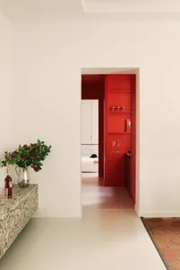 Warm and inviting kitchen with a red door, white walls, a red cabinet, and a dining table, with natural light coming in through the open door