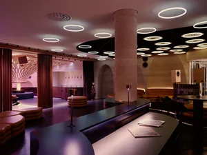 Modern restaurant with a bar and dining area featuring a variety of seating options, soft warm lighting, and neutral colors with brown and beige accents