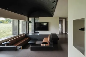 Cozy living room with a black and brown color scheme, a flat screen TV, a couch, and a dining table, featuring wood and leather materials and natural light from the windows