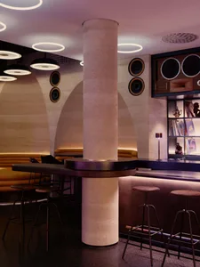 A modern bar with a mix of wood and metal materials, featuring a counter, pillar, and comfortable seating for guests