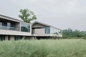 一座混凝土外牆的現代住宅，周圍環繞高草與樹木，擁有大片窗戶與寧靜氛圍