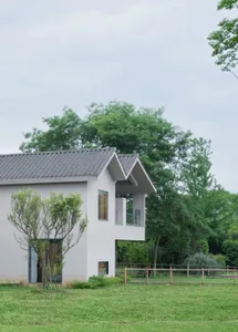 白色外觀搭配灰色屋頂的現代住宅，周圍環繞樹木，大片窗戶讓自然光線灑入空間