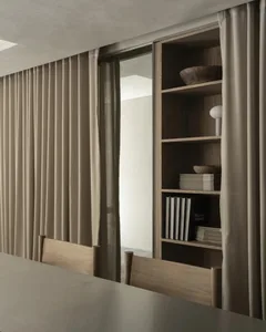 Dimly lit dining room with a wooden table and chairs, a brown curtain, and a bowl on the table