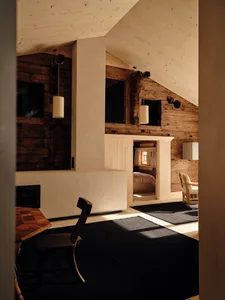 A well-lit living room with a wooden floor, a fireplace, a dining table, a couch, a chair, and a bed, giving a cozy and rustic feel