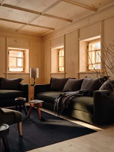 Cozy living space with wooden walls and floors, a couch, chair, and coffee table, featuring soft and diffused lighting