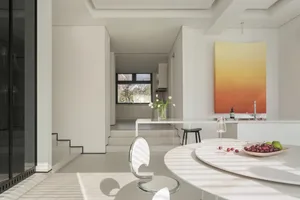 A modern kitchen and dining space with white countertops, a dining table, chairs, potted plants, and vases, in a minimalist and contemporary style