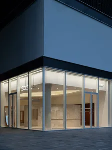 一座現代建築，擁有大型玻璃立面與白色框架，周圍環繞混凝土與自然光線