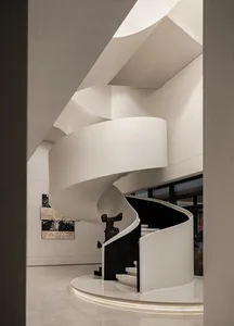 A dimly lit staircase made of white marble with a black railing in a large, modern space