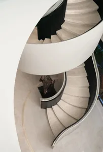 A dimly lit spiral staircase with marble steps, set in a modern building with a minimalist design