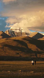 A serene mountain landscape with a snow-covered peak, surrounded by shades of gray, white, and brown, under natural sunlight