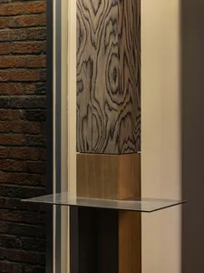 A wooden sculpture on a glass table in a dimly lit room with a brick wall