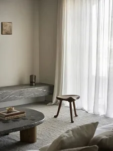 Cozy modern living space with a stone countertop, stone table, and natural light from windows, featuring a couch, chair, and coffee table