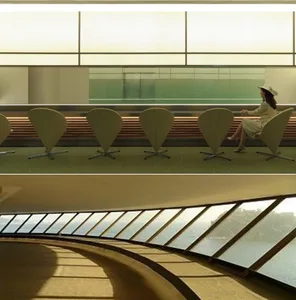 A modern lobby with a curved wall and a row of wooden chairs in a semi-circle, with a person sitting in one of them, and a large window providing natural light