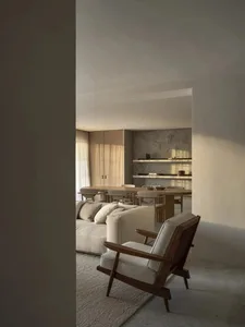 Comfortable living space with a couch, chair, and dining table, featuring wood and fabric materials, well-lit with a warm atmosphere