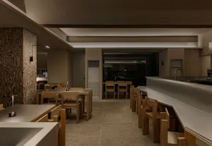 Cozy modern restaurant interior with a large dining table, kitchen appliances, and comfortable seating