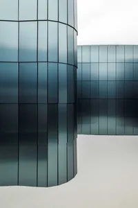 A modern building with a glass exterior, featuring a large glass wall that reflects the surrounding environment, in a contemporary and minimalist style