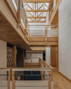 Open-plan living and dining space with wooden floors, a glass railing, and a dining table and chairs, well-lit and inviting