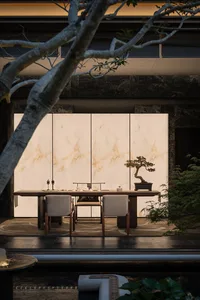 Cozy dining space with a marble table, stone wall, and dim lighting, featuring a potted plant, chairs, and a vase