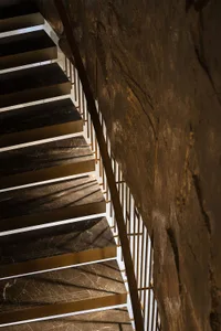 A dimly lit room with a stone wall and a staircase featuring a marble-like surface and metal details