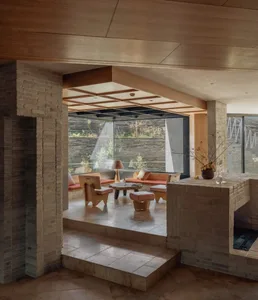 Warm and inviting living room with a stone fireplace, brick wall, stone floor, and stone countertop, furnished with a couch, chair, and dining table, with potted plants and vases adding to the ambiance