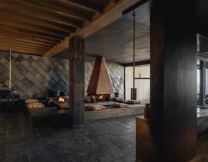 Cozy living room with a stone fireplace, stone wall, and comfortable seating areas, featuring a potted plant and modern decor