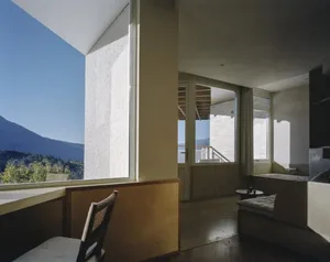 Comfortable living space with a wooden floor, a couch, a chair, and a dining table, lit by natural light from a large window