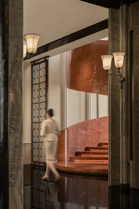 A woman in a white dress walks down a red marble staircase in a luxurious interior setting