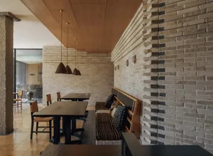 Dining room with a wooden floor, brick walls, a dining table, chairs, a couch, and various furniture pieces, lit to create a warm and inviting atmosphere