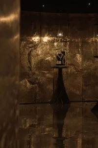 A dimly lit room with a marble floor and gold wall, featuring a black table with a trophy and a gold statue, creating a luxurious and elegant atmosphere