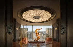 Bright and inviting lobby with a glass ceiling, a circular light fixture, a large sculpture, and a fountain, illuminated by natural light