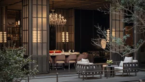 A classic dining room with a black and white color scheme, a large dining table, and comfortable seating for guests, set with wine glasses, cups, and a bowl of fruit, with natural light coming in through the windows