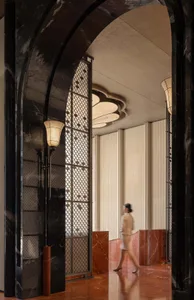 A woman walks down a hallway with marble flooring, surrounded by elegant decorations and dark tones