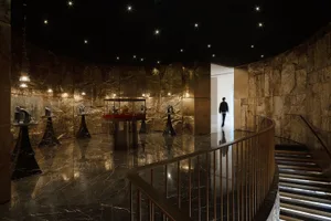 A dimly lit room with a marble floor and walls, a metal staircase, and various items on display, including jewelry