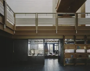 Large open living room with a wooden floor, balcony, staircase, and modern furniture, featuring a fireplace and natural light from windows