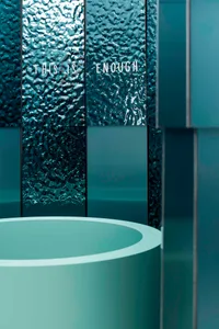 A modern bathroom with a blue-green color scheme, featuring a large round sink, blue-green walls, and floor, with dim lighting creating a relaxing atmosphere