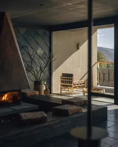 Cozy living room with a fireplace, a couch, and a chair, featuring a mix of natural and artificial lighting, and a modern functional style