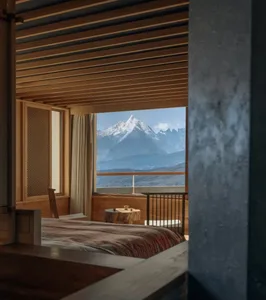 A bedroom with a bed, chair, and window, featuring wood and fabric materials in a cozy and inviting atmosphere with natural light from the window