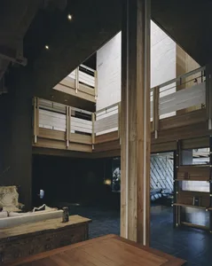 A dimly lit room with a large wooden staircase, wooden railing, and wooden table, set against a wooden wall in a modern home