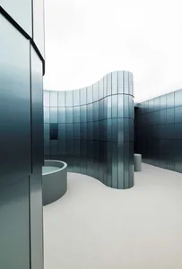 Modern building with a curved design, large glass wall, and blue interior walls, surrounded by natural light and a well-lit atmosphere