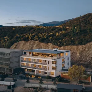 A modern hotel building with a concrete exterior, surrounded by trees and natural scenery, with soft and diffused lighting