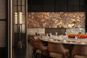 Dining room with a round table set with wine glasses, cups, and bowls, surrounded by chairs, in a room with a marble-textured wall and dim warm lighting