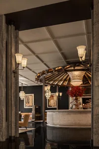 A modern bar with a circular light fixture above the counter, surrounded by chairs and bottles, in a predominantly white space with dim lighting