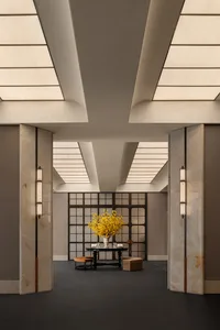 A dimly lit lobby with a hardwood floor, a white ceiling, and a large vase of flowers on a table