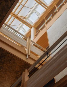 A modern building with a wooden staircase and glass ceiling, surrounded by glass walls and filled with natural light