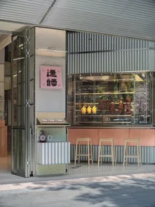 Casual restaurant with a pink and green color scheme, featuring a counter with food display, chairs, and a refrigerator in the background